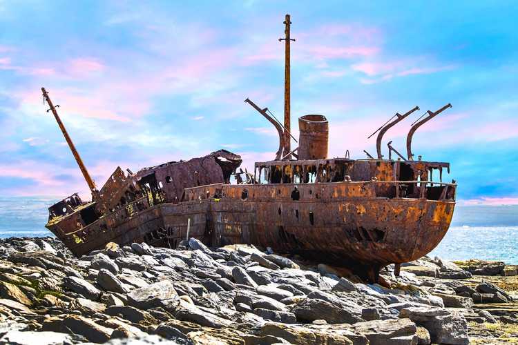 El casco oxidado e histórico del naufragio del MV Plassey descansando en la escarpada costa de piedra caliza de la isla de Inisheer bajo un impresionante cielo azul